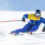 Un skieur en combinaison jaune et bleue vire sur la neige, ses skis paraboliques taillant la piste.