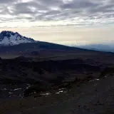 Vue sommet Kilimandjaro, paysage désertique et enneigé sous un ciel nuageux. Un randonneur solitaire sur le sentier.