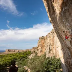 Un grimpeur défie la falaise en Sicile, avec la mer et la végétation en toile de fond. L'escalade sicile offre des vues spectaculaires.