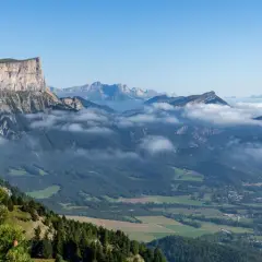Vue panoramique du Vercors en été. Des montagnes majestueuses, des nuages bas et une forêt verdoyante invitent à explorer ce paysage magnifique.