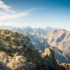 Vue spectaculaire sur la partie sud du GR20, avec des randonneurs sur un sentier rocheux et des montagnes majestueuses à perte de vue.