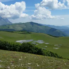 Vastes prairies verdoyantes parsemées de petits étangs dans le parc national des Monts Sibyllins, sous un ciel bleu et nuageux.