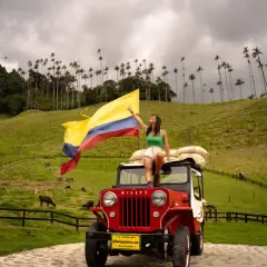 Femme sur une jeep rouge, drapeau colombien flottant, au milieu des palmiers de cire de la Vallée de Cocora, Colombie.