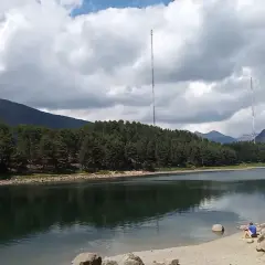 Vue paisible du lac d'Engolasters, entouré de forêts de pins et de montagnes. Deux tours de transmission se dressent à l'horizon.