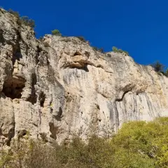 Un grimpeur jaune défie la falaise imposante, un véritable chateauvert pour l'escalade. Le ciel bleu azur surplombe ce paysage rocheux.