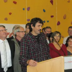 Antoine Cayrol, orateur charismatique, s'exprime devant un mur d'escalade coloré, entouré d'une foule attentive.