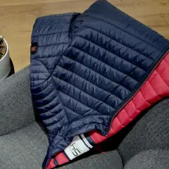 Doudoune bleu marine et rouge pliée sur un fauteuil gris. Une plante verte est posée à côté. Idéal pour redonner du gonflant à une doudoune.