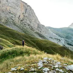 Randonneuse solitaire sur un sentier herbeux, dominant les pentes verdoyantes et les montagnes majestueuses du tour de l'Ubaye.