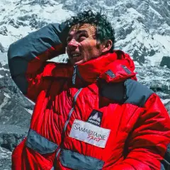 Jean-Christophe Lafaille, le visage marqué par l'effort, se protège du soleil sur fond de montagnes enneigées.