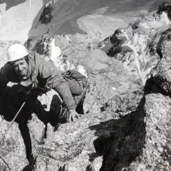 Serge Gousseault, alpiniste chevronné, escalade une paroi rocheuse escarpée, casque blanc sur la tête.