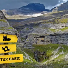 Panneau jaune indiquant "SENDITUR BASIC" dans une vallée montagneuse spectaculaire.