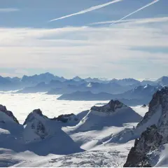 Vue panoramique d'une majestueuse montagne France enneigée, avec des sommets bleutés à l'horizon et une mer de nuages blancs.