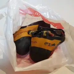 Une paire de chaussons d'escalade Sportiva jaunes et noirs, visiblement un chausson qui pue, dans un sac en plastique blanc.