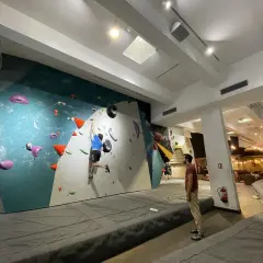 Un jeune homme en bleu pratique l'escalade sur un mur coloré, un autre spectateur l'observe. L'ambiance est propice à l'escalade nation.