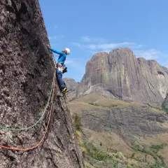 Un grimpeur en pleine ascension sur un rocher impressionnant, avec des montagnes majestueuses en arrière-plan. Une aventure d'escalade à Madagascar.