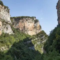 Immenses falaises rocheuses bordent le **Cañon de Añisclo**, couvertes de végétation luxuriante. Le ciel bleu clair domine.