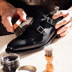 Un artisan brosse une chaussure noire à double boucle, lui redonnant son éclat. La tige de la chaussure est en cuir poli.