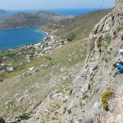 Grimpeur en action sur les falaises de Kalymnos, avec une vue imprenable sur la mer Égée et le village en contrebas.