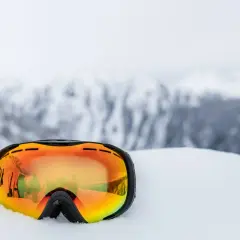 Masque de ski orange posé dans la neige, reflétant des skieurs. Indispensable pour savoir quel masque de ski choisir.
