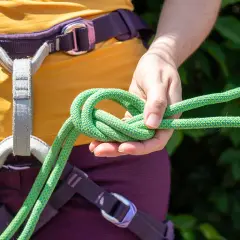 Main d'escaladeuse nouant une cordelette verte, prête pour une longe dynamique.