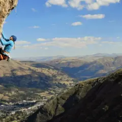 Charlotte Durif, grimpeuse audacieuse, défie la falaise rocheuse sous un ciel bleu. Paysage montagneux spectaculaire en arrière-plan.