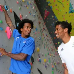 Deux grimpeurs, dont frere mawem, sourient sur un mur d'escalade coloré. L'un est en bleu, l'autre en blanc avec le logo de la France.