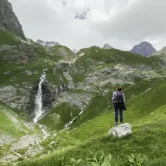 Une randonnée dans les Bauges, avec une cascade impressionnante et des montagnes verdoyantes. Une femme admire le paysage.