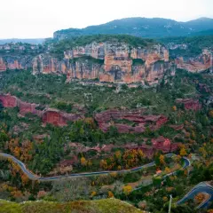 Paysage spectaculaire de falaises rouges et vertes, avec une route sinueuse traversant la vallée. Un paradis pour la siurana escalade.