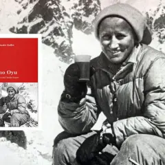 L'alpiniste Claude Kogan, souriante, tenant une tasse, sur fond de montagnes enneigées. Le livre "Cho Oyu, le destin de Claude Kogan" est visible.