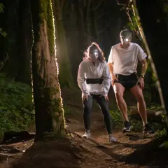 Deux coureurs équipés de lampes frontales s'aventurent sur un sentier forestier sombre. Une **randonnée nocturne** pleine d'adrénaline.