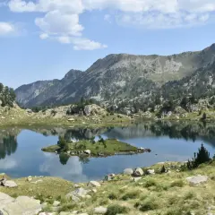 Vue paisible du cirque de Colomers, avec un lac miroir reflétant les montagnes et une petite île verdoyante.