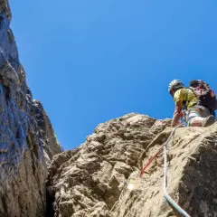 Un grimpeur en plein effort, casque et sac à dos, s'engage sur une paroi rocheuse. L'escalade dans les Pyrénées offre des vues spectaculaires.