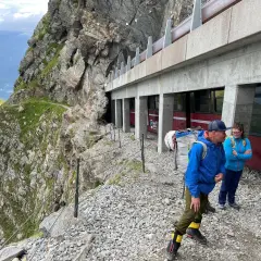 Des randonneurs se tiennent près d'un train rouge, prêts à découvrir comment se rendre au nid d'aigle par ce chemin escarpé.