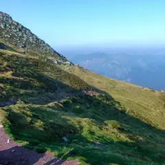 Une personne randonne seule sur un sentier de montagne, profitant d'une vue panoramique sur les vallées bleutées.