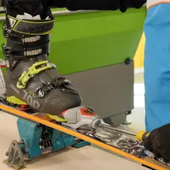 Réglage d'une fixation de ski sur un tableau de fixation. Un skieur ajuste la fixation avec un tournevis.