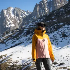 Une femme porte une veste shell colorée, idéale pour affronter les montagnes enneigées.