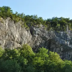 Falaise rocheuse imposante, la balme de Yenne offre un spectacle naturel saisissant, couronnée de verdure sous un ciel bleu.