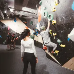 Des grimpeurs s'entraînent dans une salle de block animée, certains escaladent des murs colorés, d'autres observent.