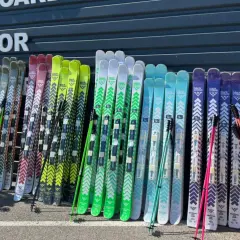 Une rangée de skis de différentes couleurs, certains avec des motifs chevron, prêts pour le freeride. La **taille ski freeride** varie pour s'adapter à tous les riders.