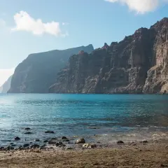 Les falaises de Los Gigantes se dressent majestueusement au-dessus de l'océan bleu. Le rivage est couvert de sable et de galets.