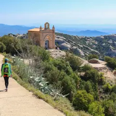 Une randonnée à Montserrat, avec une femme portant un sac à dos et une corde, menant à une petite chapelle perchée sur une colline rocheuse.