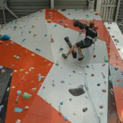 Un grimpeur s'entraîne pour **climb up** sur un mur d'escalade intérieur aux couleurs vives, utilisant des prises variées.
