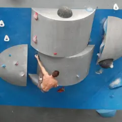 Un grimpeur s'accroche à un bloc escalade, défiant la gravité sur un mur bleu.