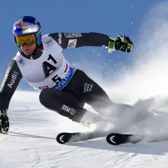Un skieur acrobatique en plein virage, projetant de la neige avec ses skis rocker. Casque Red Bull, combinaison Colmar.