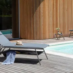 Chaises longues Lafuma près d'une piscine, avec une serviette bleue et un chapeau de paille. Ambiance détente estivale.