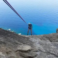 Un grimpeur se prépare pour une descente en rappel au Cap Canaille, avec la mer d'un bleu intense en contrebas. L'escalade offre une vue spectaculaire.