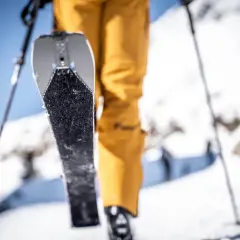 Un skieur en pantalon jaune se prépare à gravir une pente enneigée, sa peau de phoque prête à adhérer à la neige.