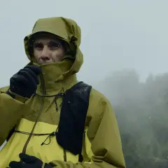 Un homme en veste Gore-Tex jaune et verte, sous la pluie, ajuste son col. Le lavage de cette veste est essentiel pour maintenir son imperméabilité.