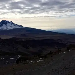 Vue sommet Kilimandjaro, paysage désertique et enneigé sous un ciel nuageux. Un randonneur solitaire sur le sentier.