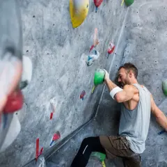 Un grimpeur concentré sur un mur d'escalade, cherchant la prise parfaite. Une scène d'escalade qui pourrait bien finir en humour si la prise glisse !